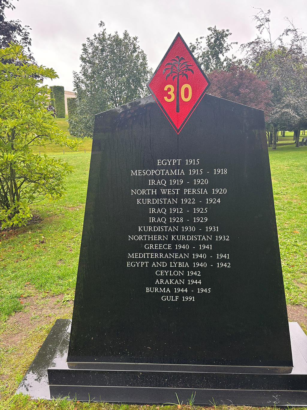 The Number 30 Squadron memorial stone with battle honours engraved upon it. At the top of the stone, at its centre, is a depiction of a Squadron emblem... A black edged red diamond, with a black palm tree, and a figure 3 and a 0, either site of the tree trunk.